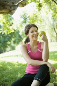 Smiling woman in activewear holding an apple promoting health and wellness